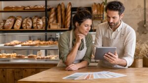 Deux responsables de boulangerie consultent une tablette au comptoir devant des pains et des viennoiseries.
